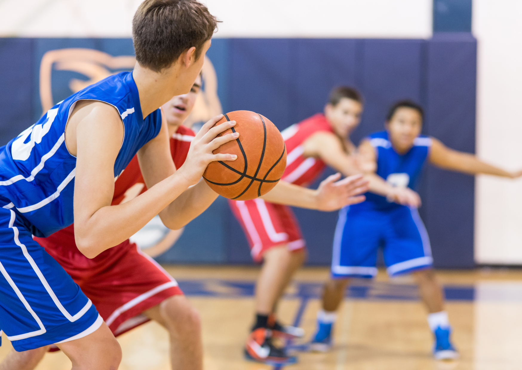 Photo of teenagers playing basketball in red and blue jerseys