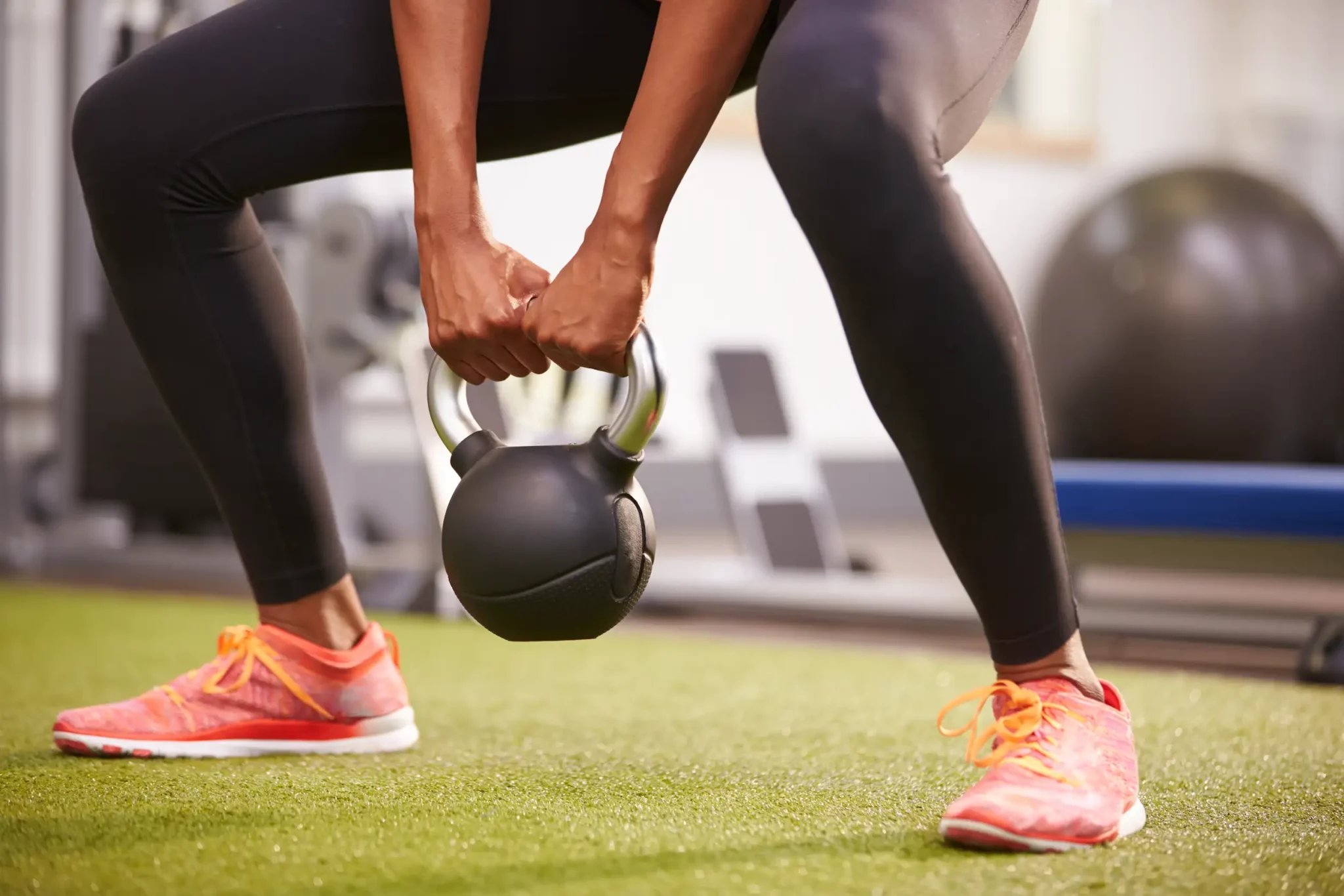 Woman in orange sneakers squats with kettlebell